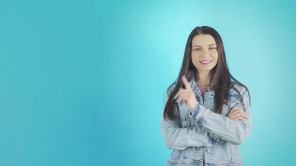 Молодая улыбающаяся женщина в джинсовой куртке бросает пальчики на голубом фоне — стоковое видео