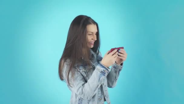 Молодая улыбающаяся женщина в джинсовой куртке играет на телефоне — стоковое видео