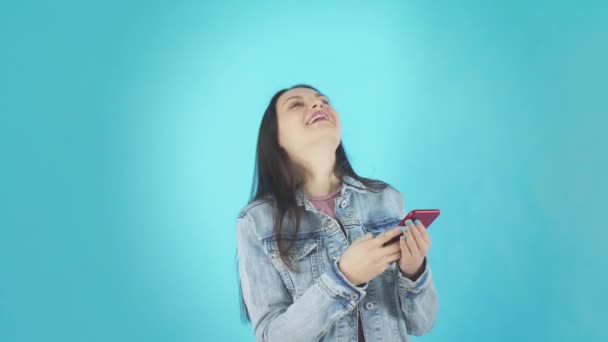 デニムジャケットの若い女性は青の背景にスマートフォンにメッセージを書きます — ストック動画