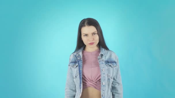 A young Disgruntled Woman in a Denim Jacket Looks at the Camera on a Blue Background — Stock Video