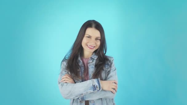 Улыбающаяся загадочная женщина в джинсовой рубашке смотрит в камеру на синем фоне — стоковое видео