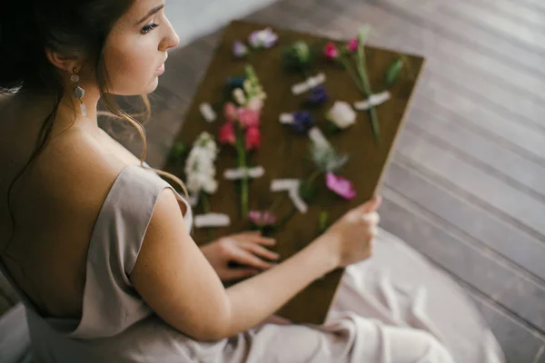 Девушка в розовом платье смотрит на свежие цветы на доске — стоковое фото