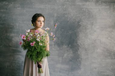 Pembe elbiseli genç bir kız Gri bir arkaplanda narin bir çiçek buketi tutuyor