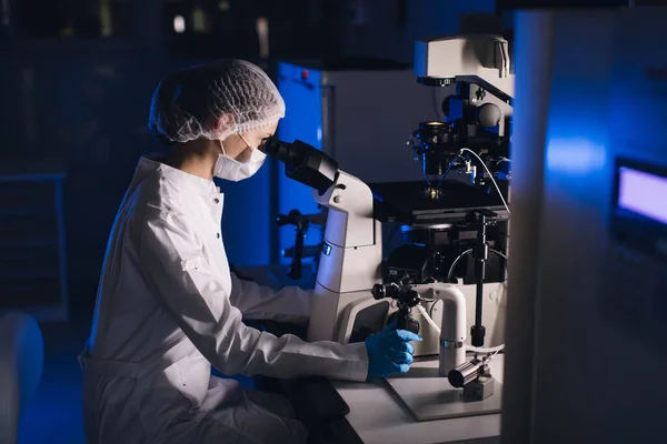 In a Modern Laboratory Scientist Conduct Experiments. Cientista chefe de pesquisa ajusta espécime em um prato de Petri e olha para ele no microscópio . — Fotografia de Stock