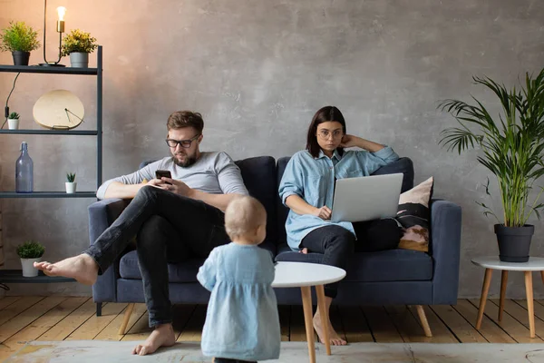 Una joven pareja en el sofá son apasionados por Gadgets. Los niños pequeños juegan alrededor de sus padres. Foto social . — Foto de Stock
