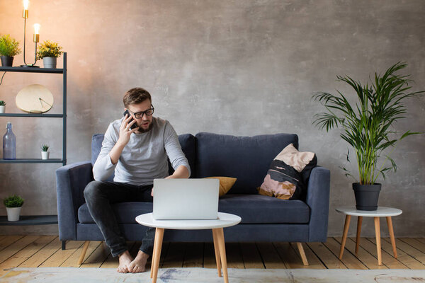 Young man in glasses angry talking on the phone sitting on the couch. Young businessman.