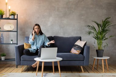 Gözlüklü, kızgın genç bir kadın telefonda kanepede oturuyor. Genç iş kadını..