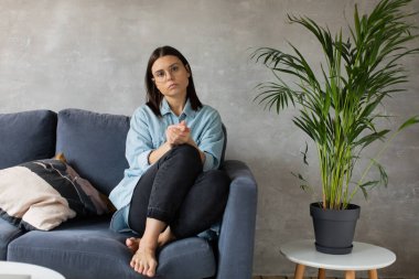 Genç bir kadın koltukta oturuyor ve kameraya bakıyor. Kız endişeli, Hüzünlü. Depresyon.