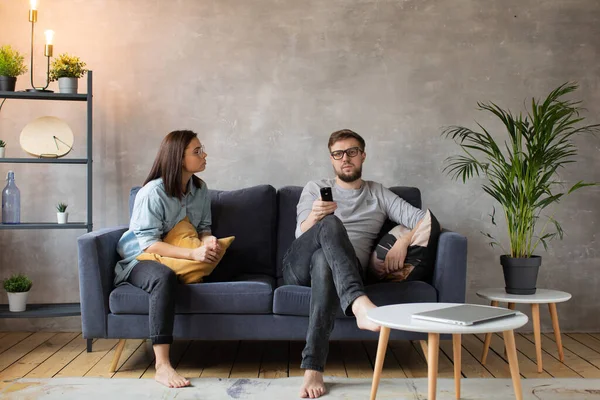 Pareja joven sentada en casa en el sofá. Man Watch TV. Mujer joven llama a su marido, él no escucha — Foto de Stock