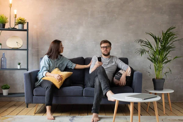 Junges Paar sitzt zu Hause auf der Couch. Mann schaut Fernsehen. Junge Frau ruft ihren Mann an, er hört nicht — Stockfoto