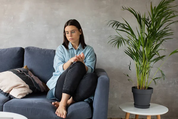Una joven mujer está sentada en el sofá mirando a la cámara. La chica está preocupada, triste. Depresión . — Foto de Stock