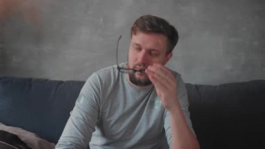 Gözlüklü genç sakallı bir adam kameraya bakıyor.