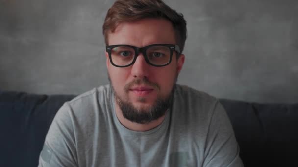 Un joven barbudo con gafas mira a la cámara — Vídeo de stock