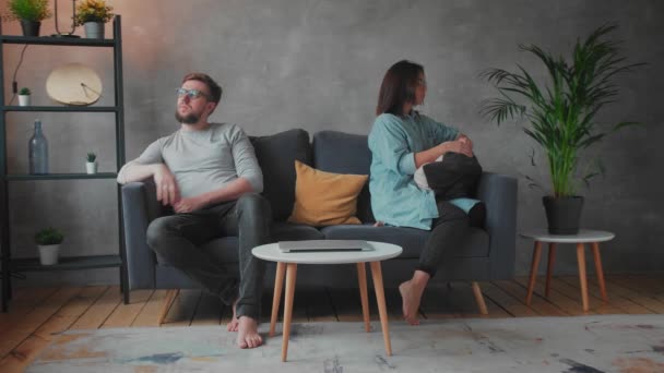 Un jeune couple est assis sur le canapé après une dispute à la maison. Le mari et la femme s'assoient l'un à côté de l'autre. Vidéo sociale . — Video