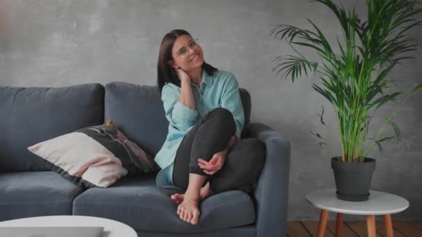 Una giovane donna è seduta sul divano a guardare la telecamera. La ragazza è felice . — Video Stock