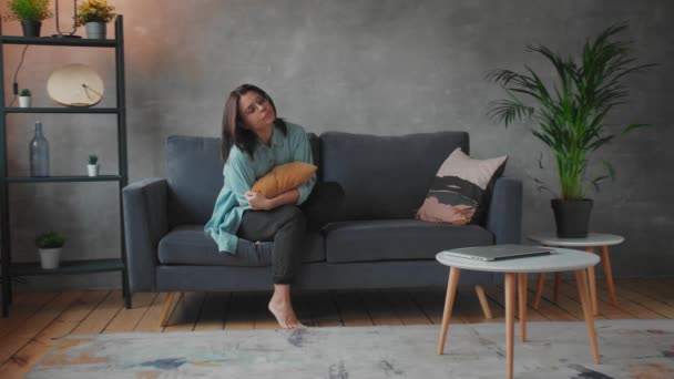 A young Girl is Sitting on the Sofa Hugging a Pillow. Depressed and Upset Woman. Social video — Stockvideo