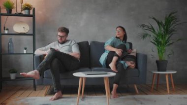 Kanepede oturan genç bir çift. Bir adam ve bir kadın telefonlarda oturuyor. Çocuk ebeveynlerin yanında oynuyor, anne ve baba çocuğa dikkat etmiyor..