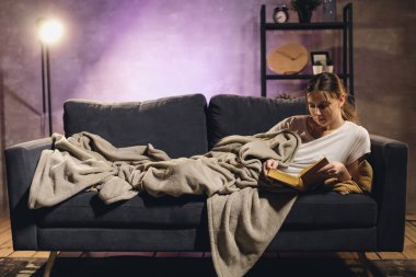 Kitap okuyan genç bir kız. Kız kanepede yatıyor. Samimi bir oda. Kız rüyaları