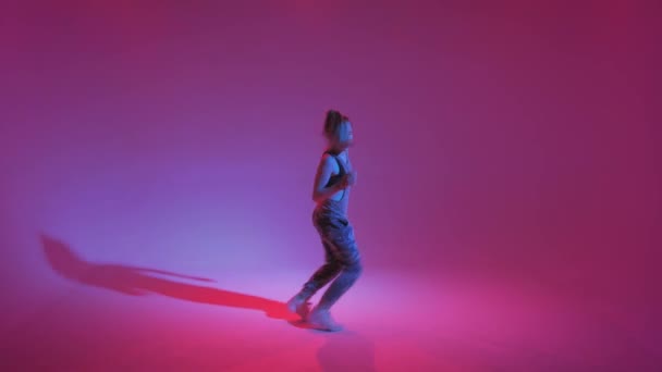 Молодая стильная девушка танцует в студии на цветном неоновом фоне. Дизайн музыкального плаката . — стоковое видео