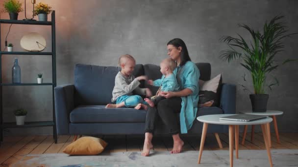Jovem mãe brincando com crianças no sofá. família feliz. conforto em casa . — Vídeo de Stock
