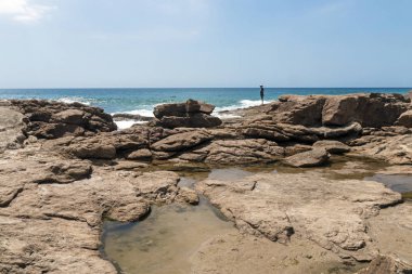 Erken sabah plajda kayalar üzerinde duran bir kişi