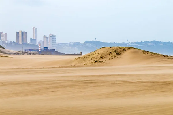 Vento pesado soprando areia na praia contra o horizonte da cidade — Fotografia de Stock