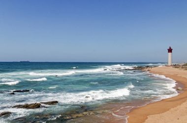 Kırmızı ve beyaz deniz feneri ile kıyı deniz manzarası gökyüzü mavi