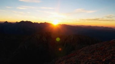 Dağ zirveleri üzerinden günbatımı Timelapse. Güneş keskin doruklarına Alpler aşağı gider. Pembe mor gökyüzü. Kamera renkli flare lens.