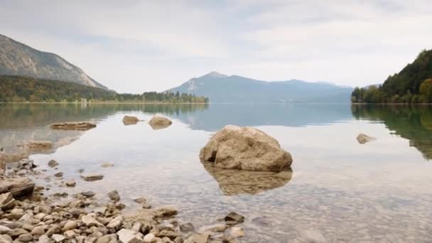 Zeitraffer-Video von Stein im Wasser des Bergsees. Sanfte Wellen am Herbstsee, Waldinseln und hohe Berge im Hintergrund. — Stockvideo