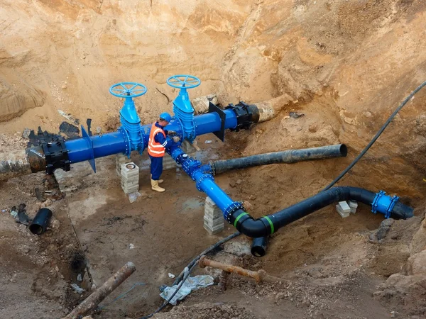 Technical expert underground at  gate valve on 500mm drink water pipes joined with new black waga multi joint members into old pipeline system. Check of repaired piping before covering by clay. Asphalt isolation