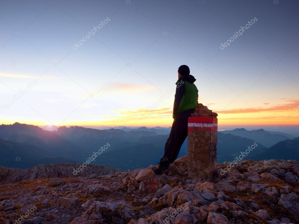 Tired hiker sit on border stone on Alps mountain. Austria Germany border. Daybreak above foggy valley