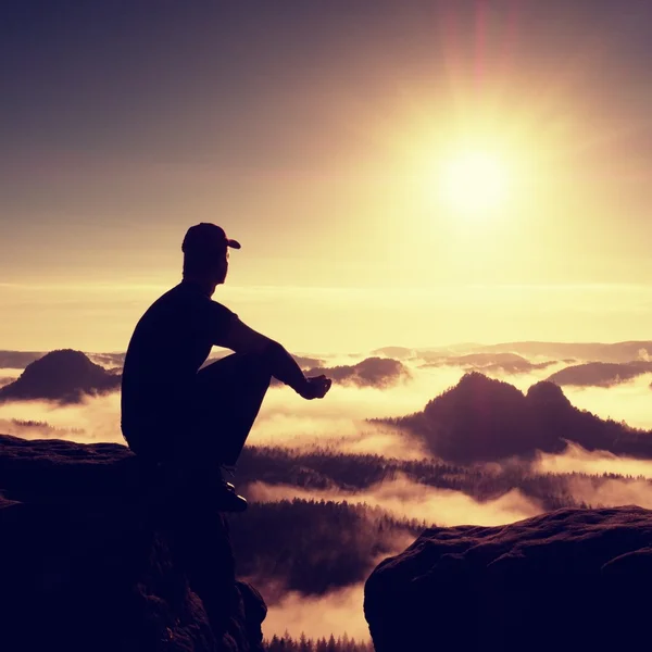 Moment of loneliness. Man with cap sit on mountain and watch to fog — Stock Photo, Image