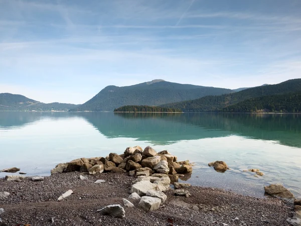 大きな岩が滑らかな湖水位から突き出ています。緑の青い水 — ストック写真