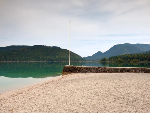 Stony sporty port at mountain lake. End of wharf with empty pole without flag. Dark blue clouds — Stock Photo, Image