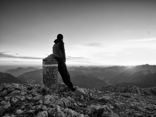 Tired hiker sit on border stone on Alps mountain. Austria Germany border. Daybreak above foggy valley