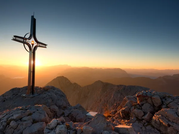 Cross raised  at mountain summit  in Alps. Sharp peak, daybreak Sun — Stock Photo, Image