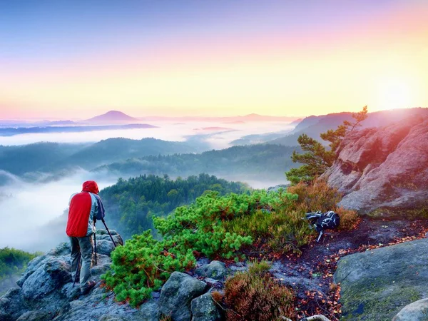 Fotograf se vyfotí s zrcadlový fotoaparát a stativ na vrcholu skály. Na podzim Pogy krajina, jaro oranžové růžové mlhavé svítání v údolí dole. — Stock fotografie