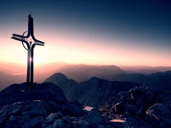 Cross raised  at Alpine mountain peakSharp rocks, Sun in sky. — Stock Photo, Image