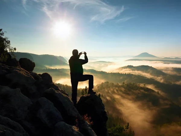 Wanderer fotografieren ein nebeliges Tal von einem felsigen Gipfel aus. Mann auf Klippe — Stockfoto