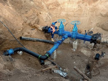Worker underground at gate valve on drink water system clipart
