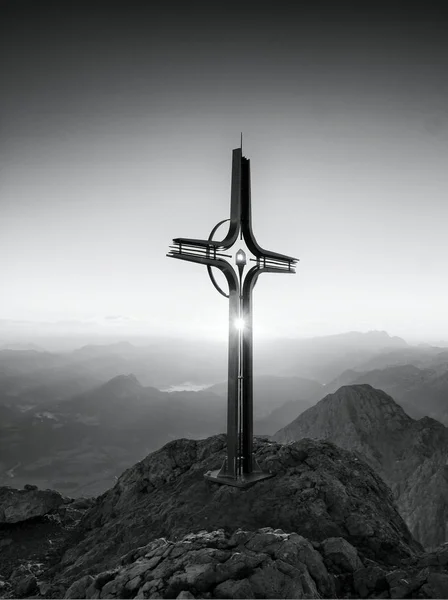 Stalen kruis op de berg in de Alpen. Scherpe rotsachtige top, daybreak zon in de lucht. — Stockfoto