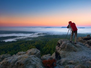 Fotoğrafçı ayna kamera ve tripod fotoğraf kaya tepe üzerinde alır. Sonbahar adamlara manzara, Bahar Turuncu pembe puslu sunrise güzel Valley aşağıdaki.
