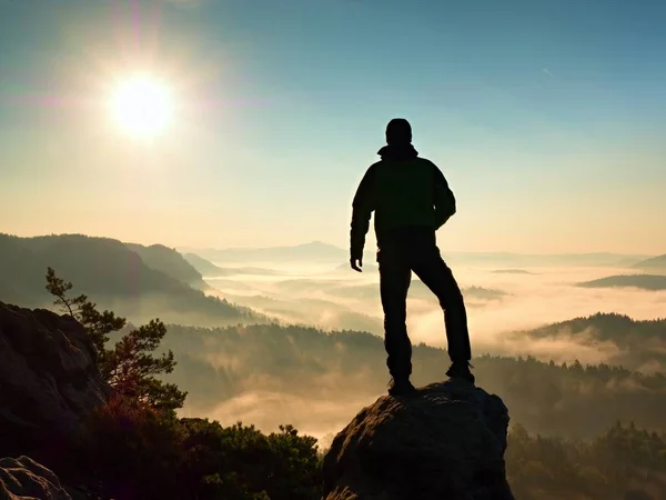 ハイカーは、渓谷の上の岩のピークに登った。朝霧と霧の谷の上の人の時計 — ストック写真