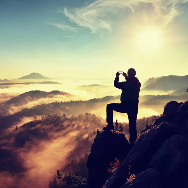 Wanderer fotografieren ein nebeliges Tal von einem felsigen Gipfel aus. Mann auf Klippe — Stockfoto
