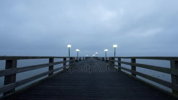 Time-lapse. Oude houten mol boven herfst Oostzee langzaam gaan. Koude mistige ochtend, zachte grizzling. Shinning gestyled straat verlichting plotseling uit te schakelen. Donkere wolken vliegen in de lucht. Dranske, Duitsland — Stockvideo