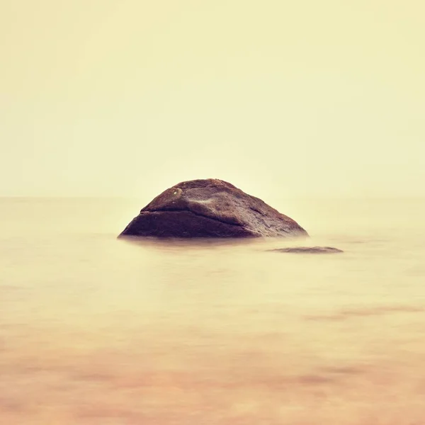 Romantische zee. Grote boulder uitsteekt uit glad golvende zee — Stockfoto