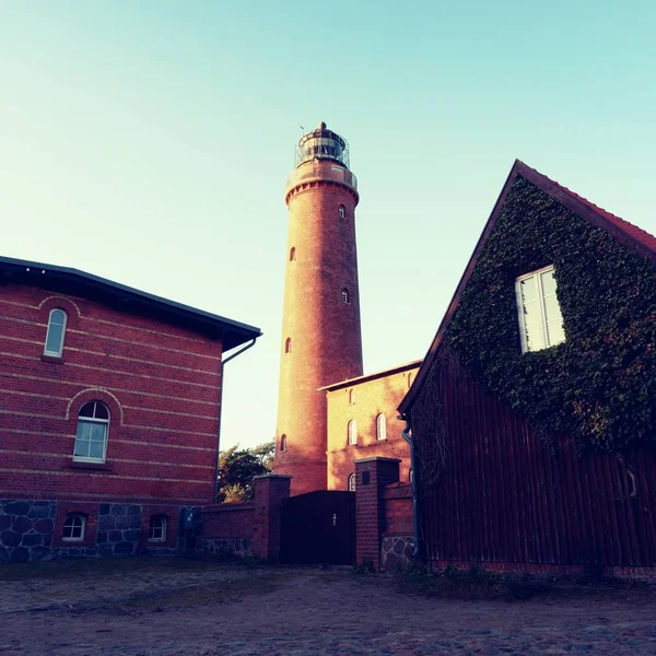 Faro viejo que brilla sobre las casas antes del atardecer. Torre iluminada con luz de advertencia fuerte —  Fotos de Stock