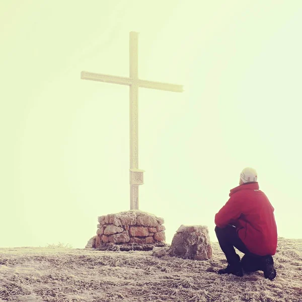 Tourist in heavy fog at cross memorial on mountain peak. Man is watching into misty Alpine valley bellow. Metal cross at a mountain peak. — Stock Photo, Image