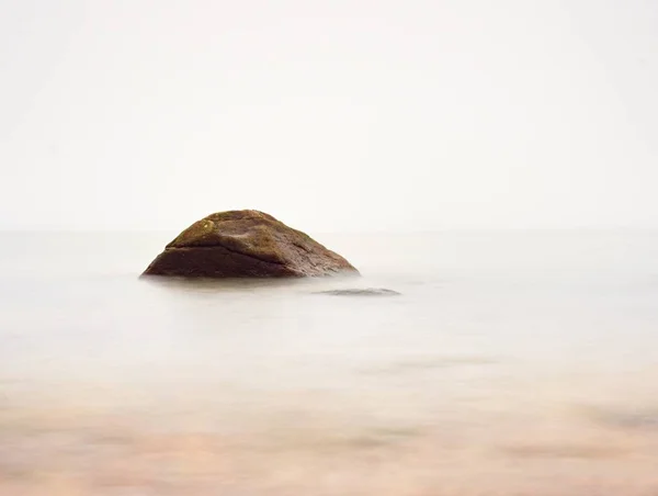 Romantický moře. Velký balvan trčí z hladké vlnité moře — Stock fotografie