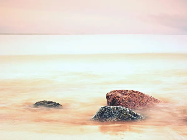 Long exposure of sea and big boulders sticking up from water within twilight time. — Stock Photo, Image